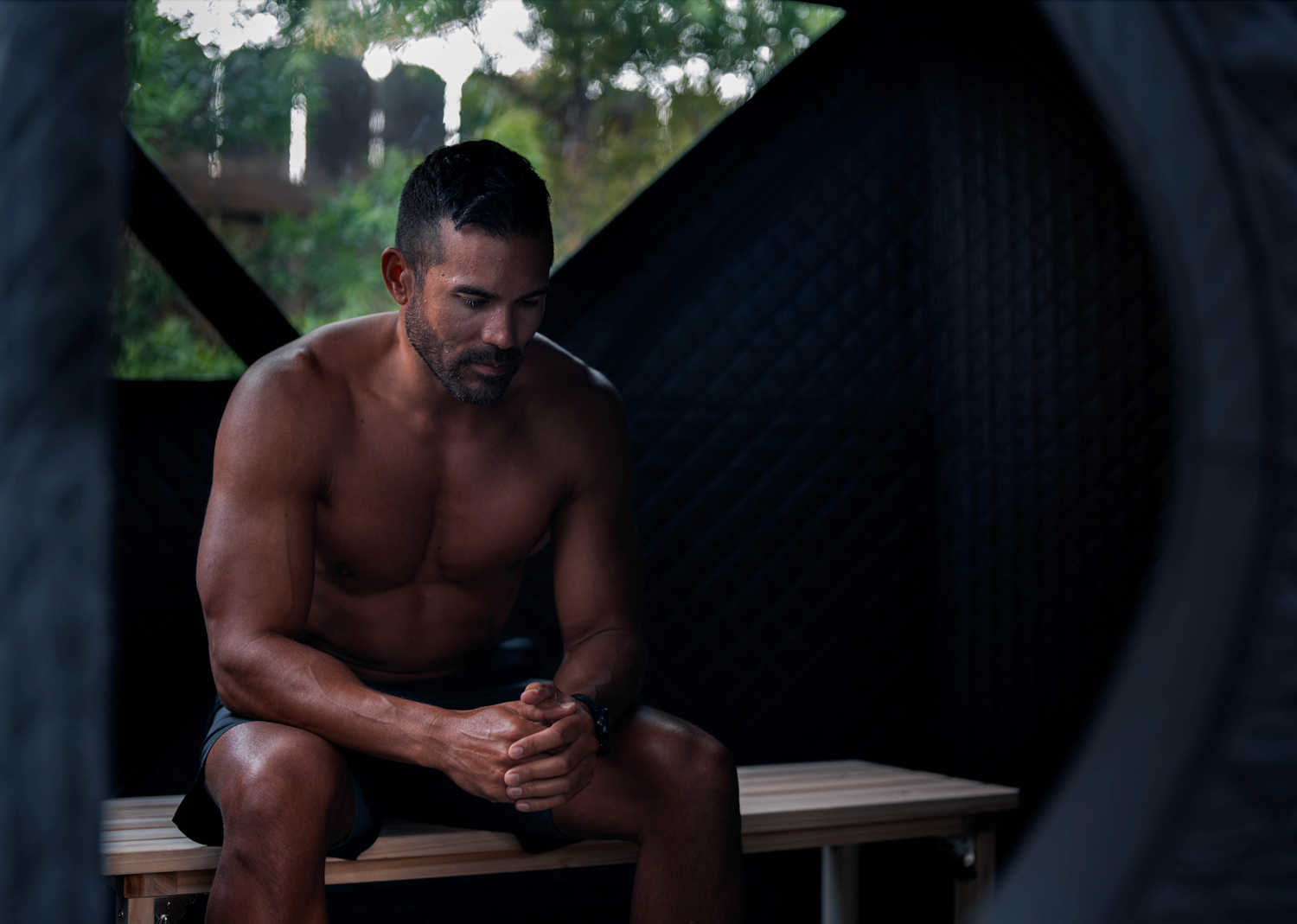A fit man with no shirt on sitting in a Sweat Tent portable sauna